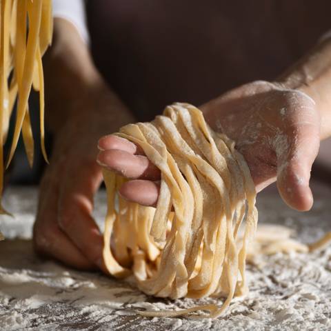 En hånd fremviser bånd af frisklavet pasta.