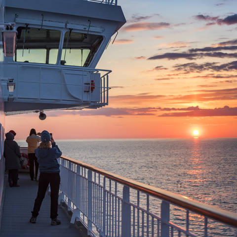 Udsigt til den norske midnatssol fra rælingen på et skib fra Hurtigruten.