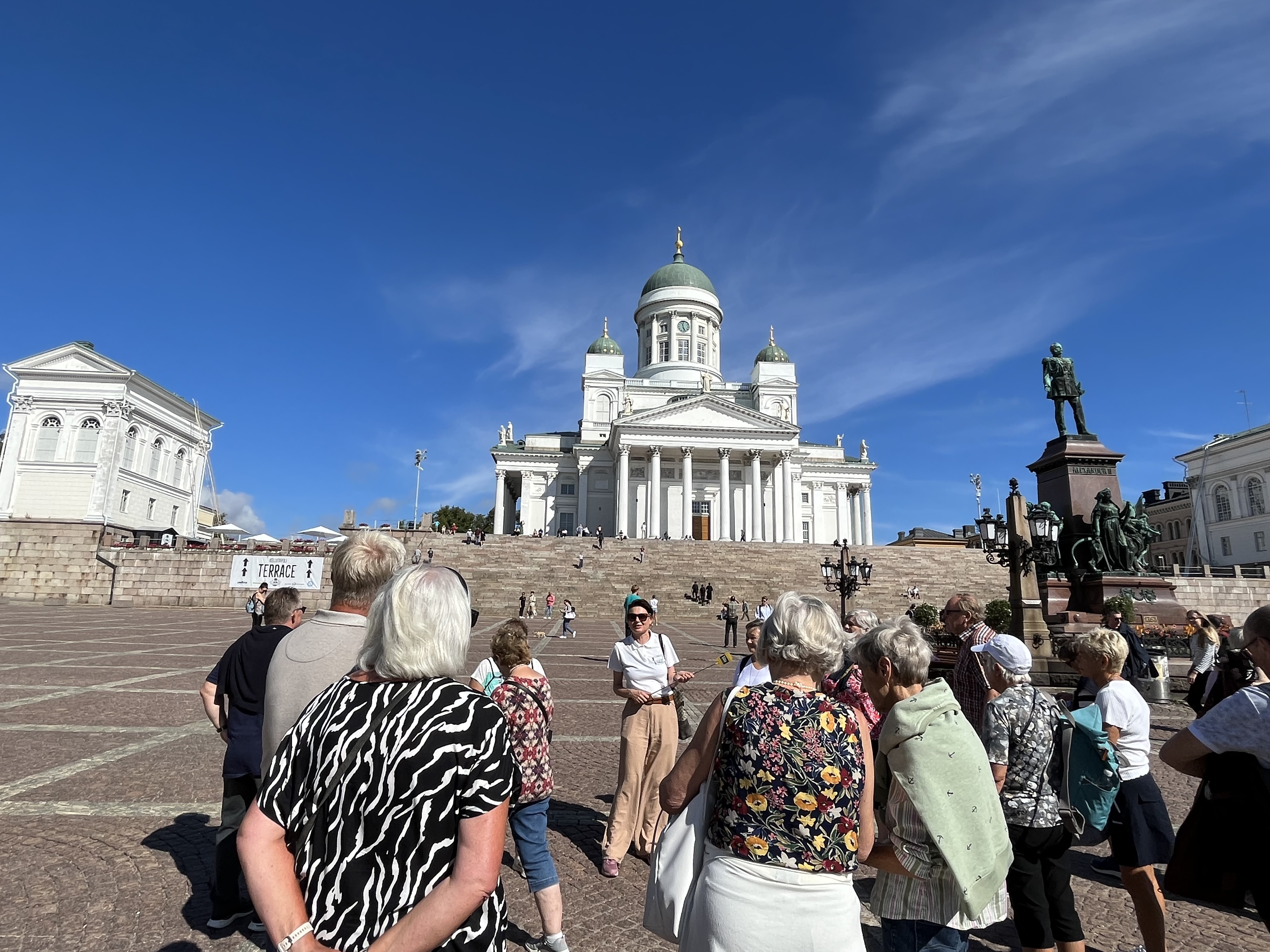 En gruppe gæster lytter til en rejseleder fra Vitus Rejser, der fortæller om domkirken i Helsinki, som de står foran.