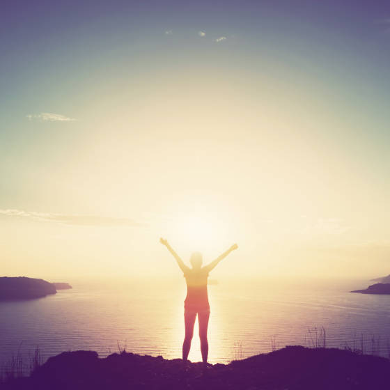 Person med armene i vejret nyder udsigten og solnedgangen over havet.