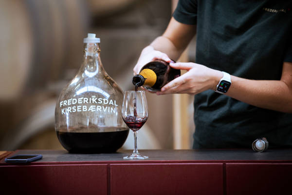 Servering af en smagsprøve i et vinglas hos Frederiksdal Kirsebærvin på Lolland i Danmark.