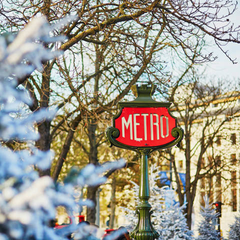 Gammelt skilt til Metroen med snedækkede træer i forgrunden i Paris i Frankrig.