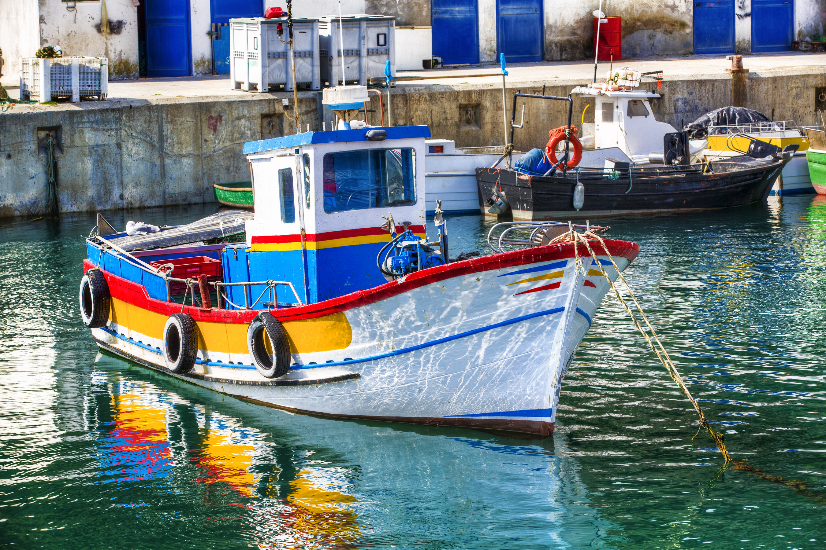 Farvestrålende lille fiskerbåd i havnen i Sesimbra i Portugal.