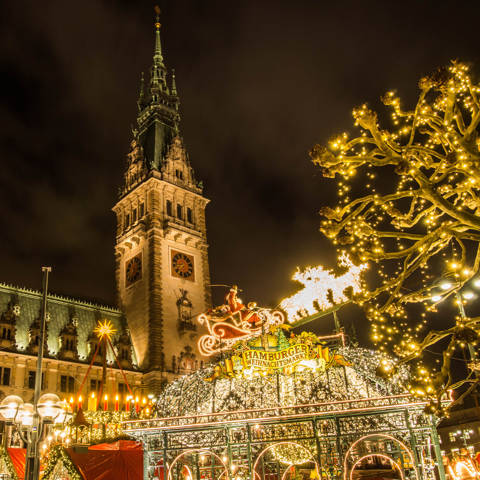 Aftenbillede med indgangsporten til Hamburger Weihnachtsmarkt og rådhuset i baggrunden.