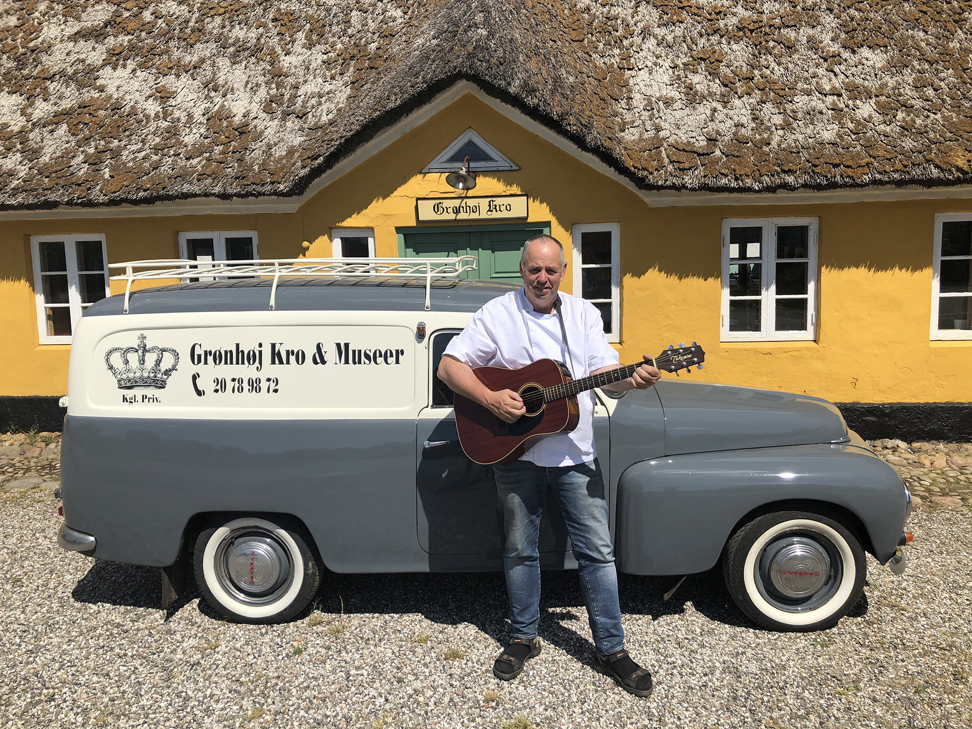 Krofatter Gregers med sin guitar og en veteranbil foran Grønhøj Kro.