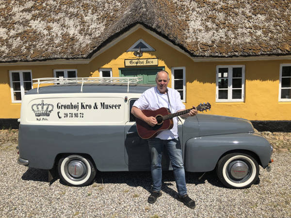Krofatter Gregers med sin guitar og en veteranbil foran Grønhøj Kro.