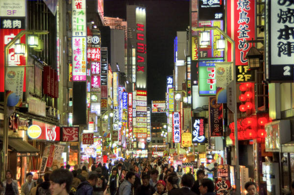 Menneskemylder og neonskilte om aftenen på en gågade i Tokyo i Japan.
