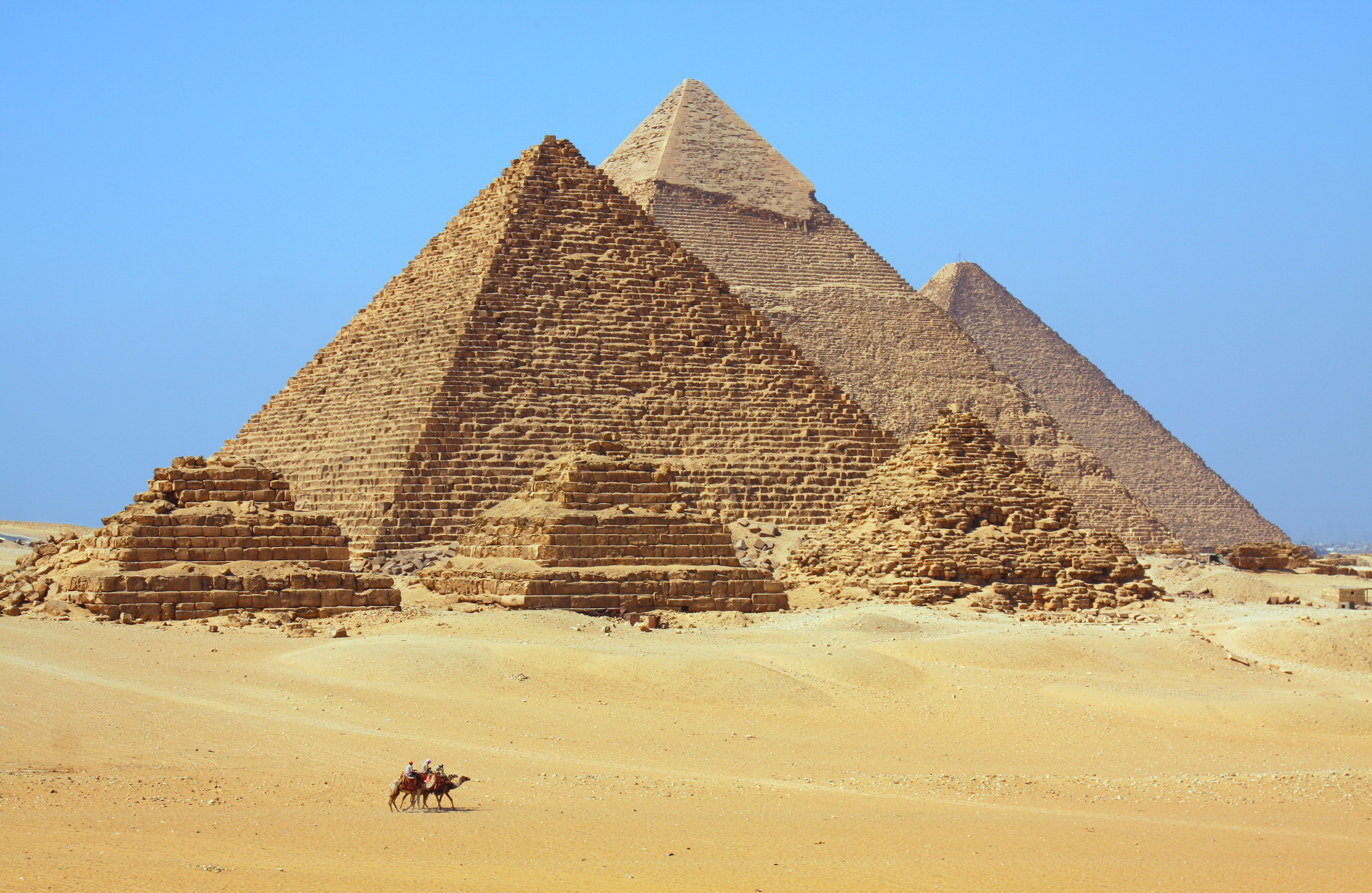 To kameler med ryttere ser meget små ud foran pyramiderne ved Giza i Egypten.