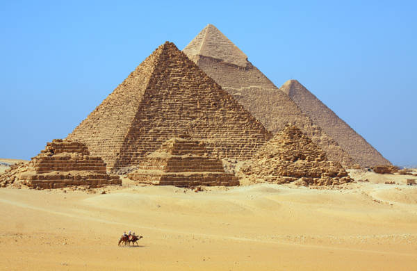 To kameler med ryttere ser meget små ud foran pyramiderne ved Giza i Egypten.